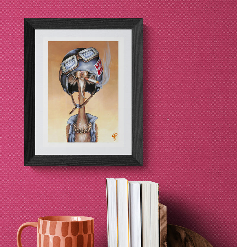 Framed artwork of a cat wearing goggles and a helmet on a pink wall.