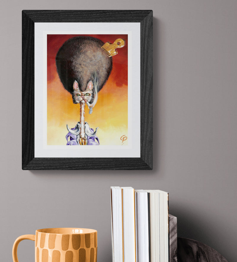 Framed artwork of a cat with a sword on a gray wall above books and a mug.