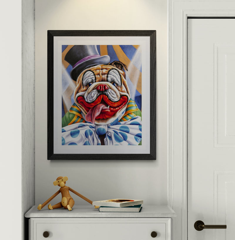 Framed artwork of a clown bulldog on a wall above a white cabinet with a toy and books.