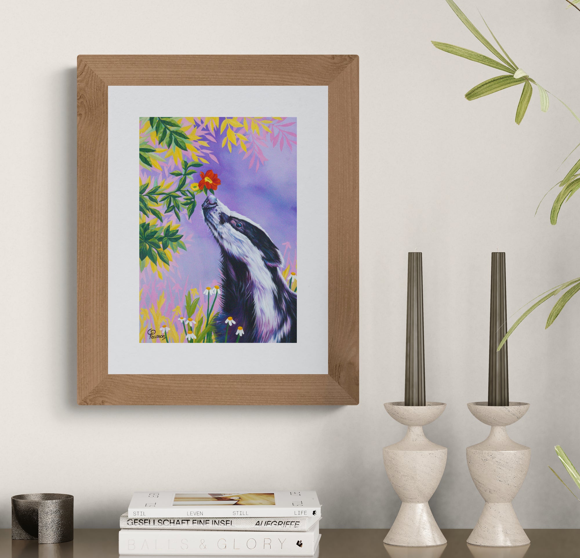 Framed artwork of a Badger with flowers on a wall above books and candle holders.