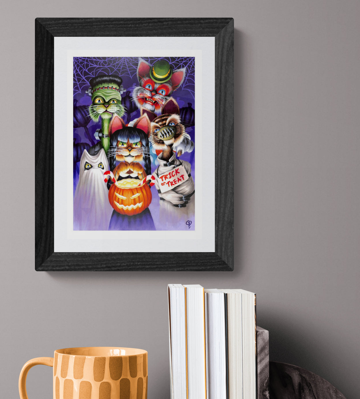 Framed Halloween-themed artwork of cats with a mug and books on a gray surface