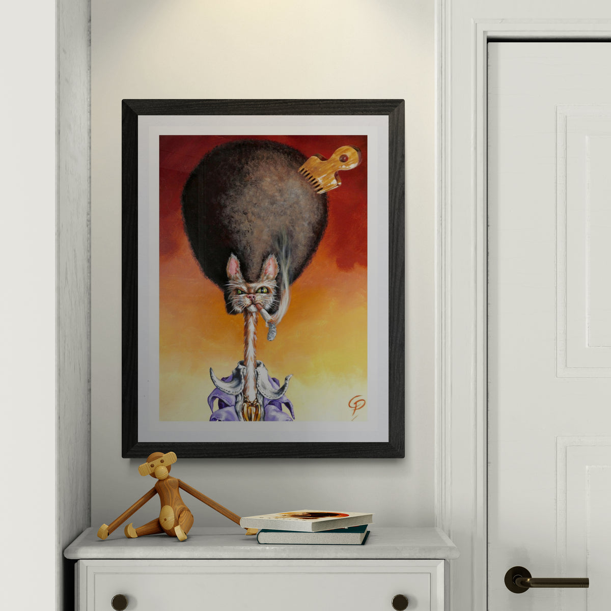 Framed artwork of a cat playing a guitar on a wall above a white dresser with a small figurine and books.