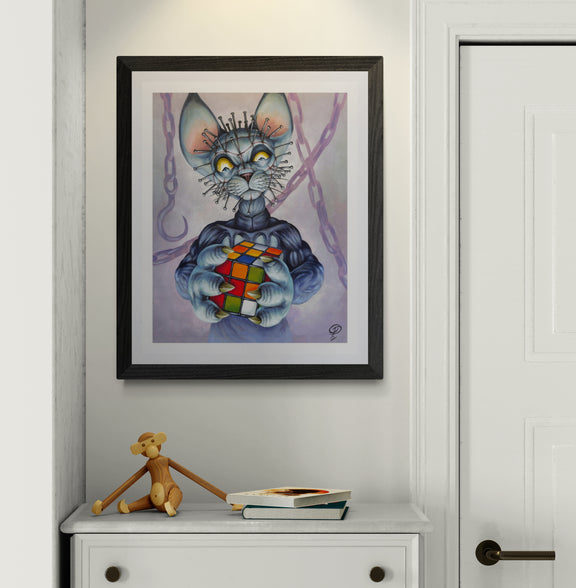 Framed artwork of a cat with a Rubik's Cube on a white wall above a cabinet.