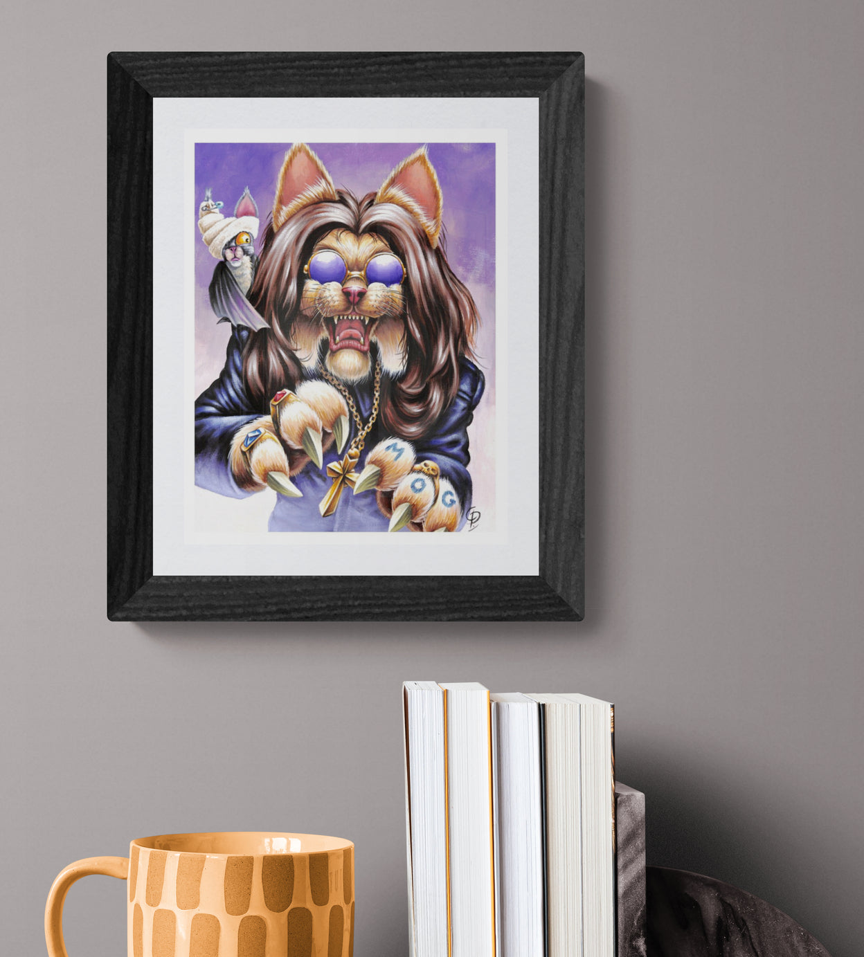 Framed artwork of a stylized cat character with a purple background, displayed on a gray wall with books and a mug below.